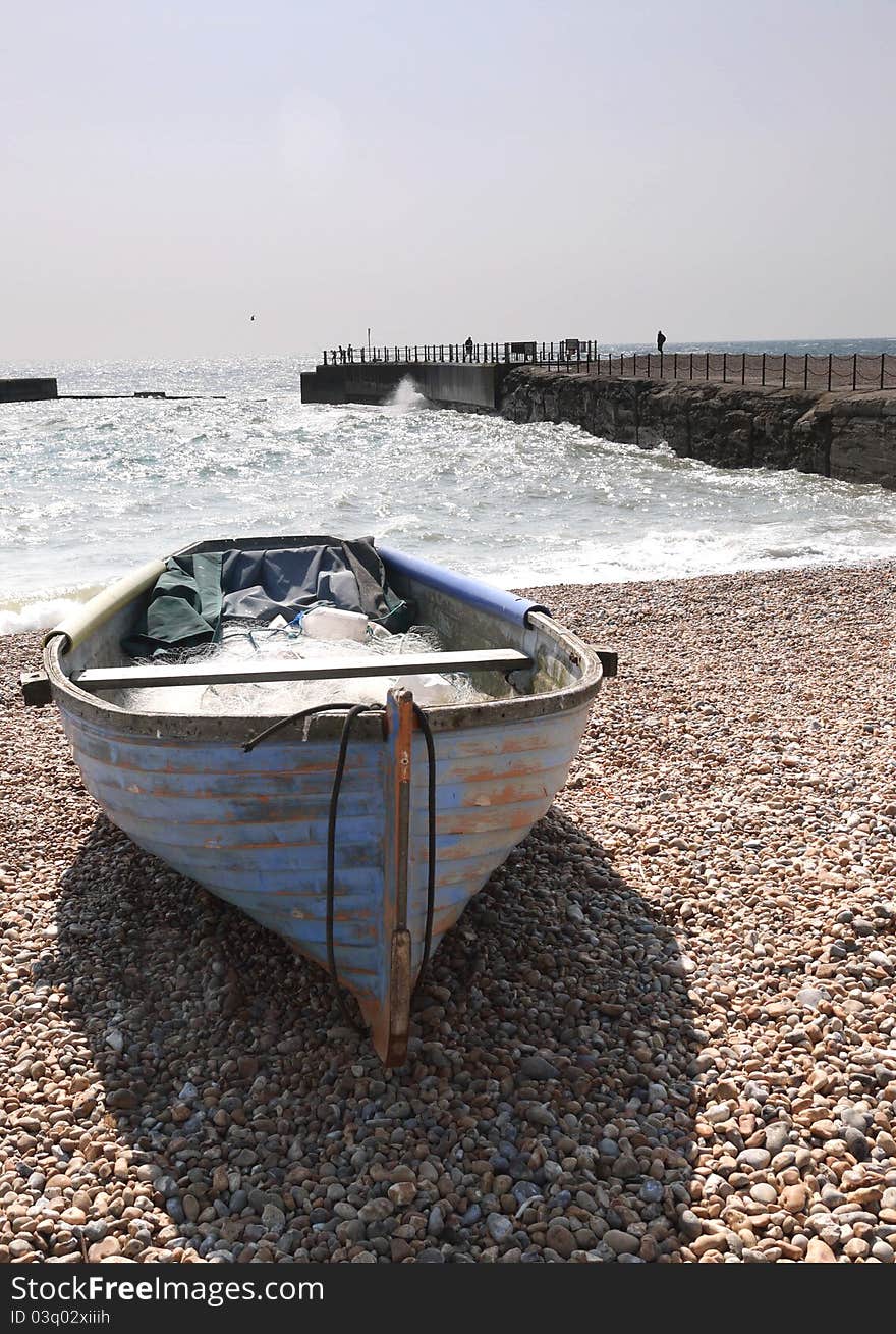 An old fishing row boat on the shore line of a pebbled beach