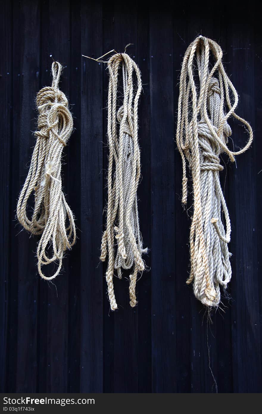 Three-strand twisted natural fibre rope hanging on black wooden wall. Three-strand twisted natural fibre rope hanging on black wooden wall.