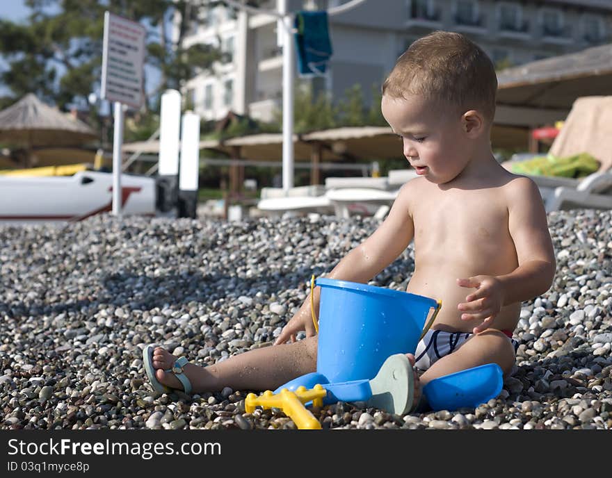 One and half year old child sitting on the pebble beach. One and half year old child sitting on the pebble beach