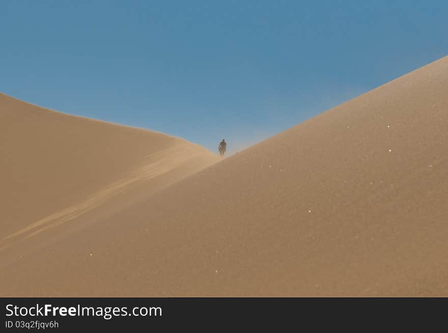 Wind blowing in high dunes in the Namib desert with a man's figure high above. Wind blowing in high dunes in the Namib desert with a man's figure high above