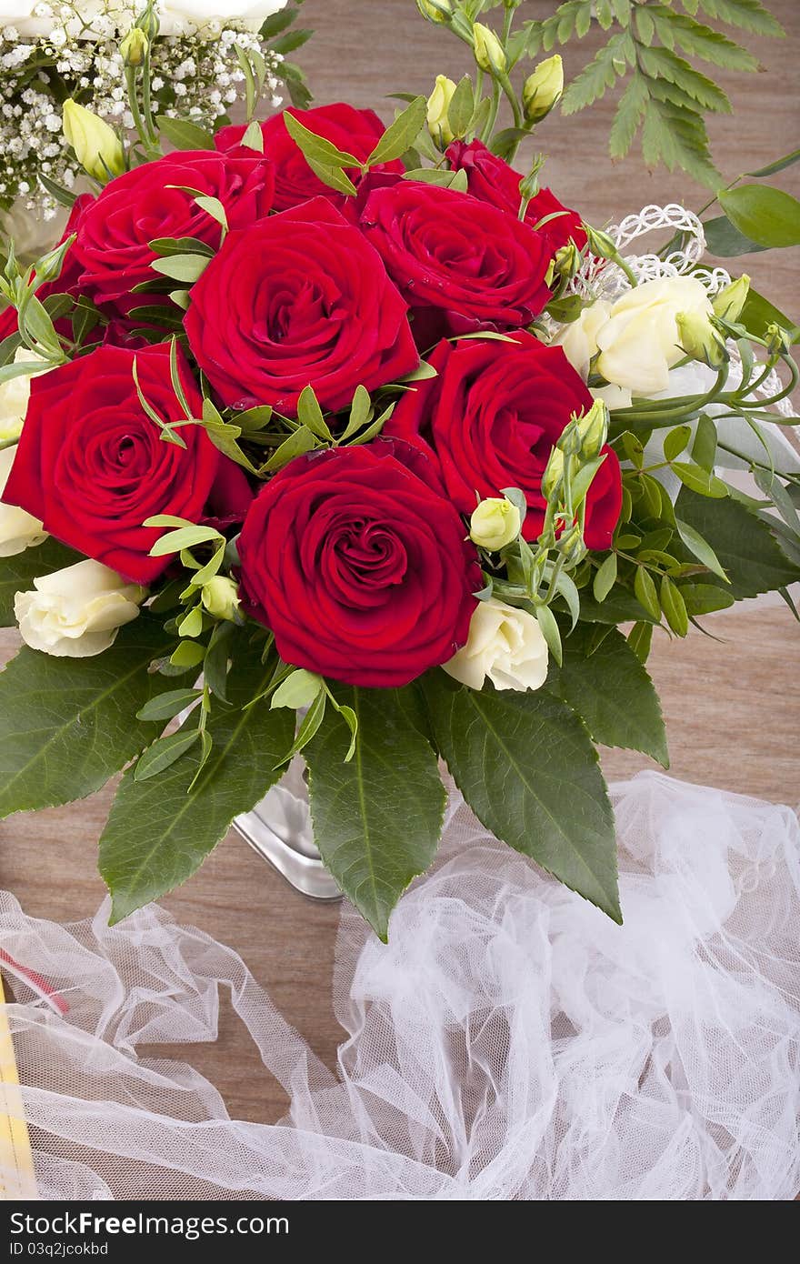 Studio-shot of a bridal bouquet with red and white roses on a wooden tray.