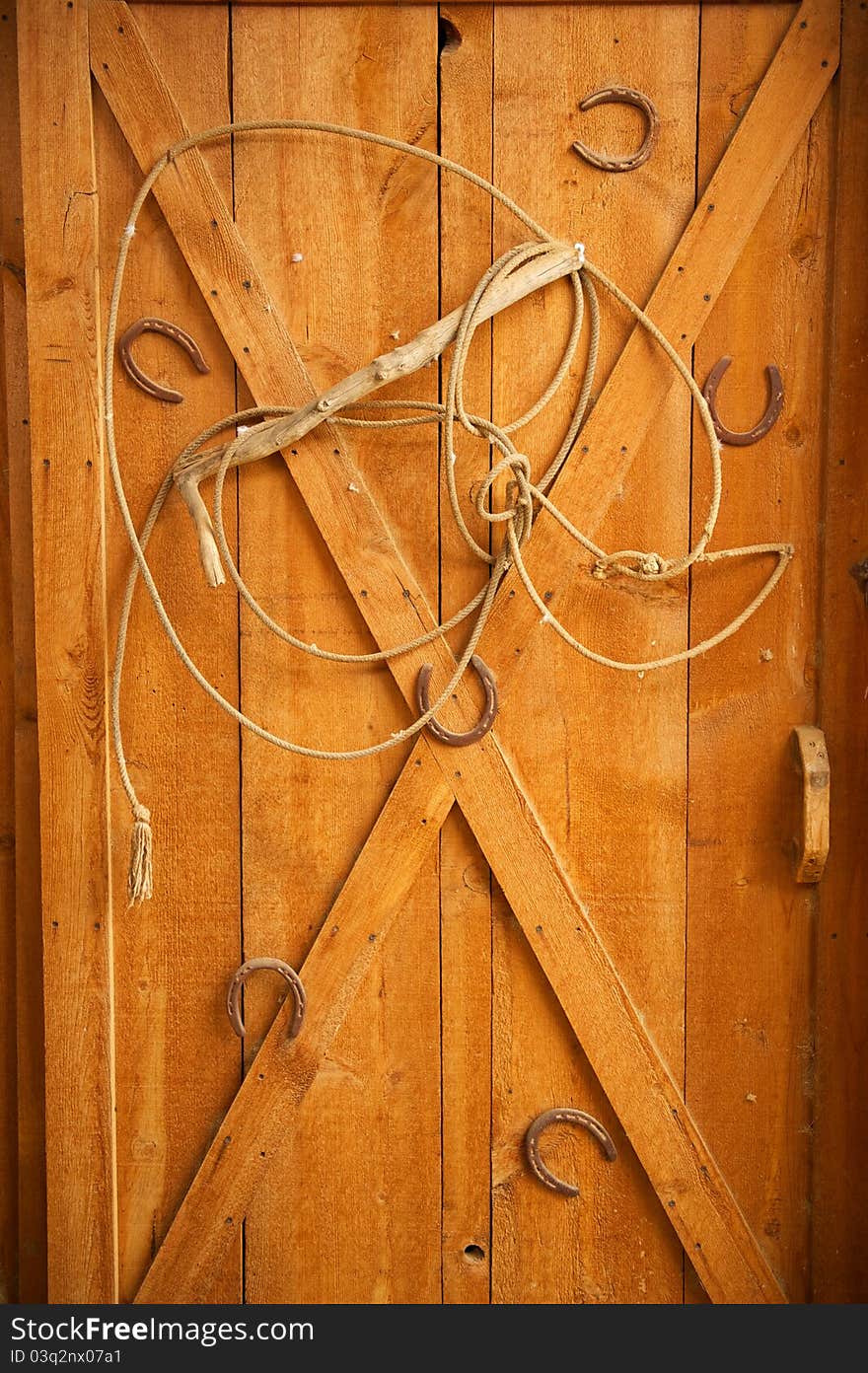 An old lasso is arranged in a decorative way with old rusted horse shoes on a golden wooden door. An old lasso is arranged in a decorative way with old rusted horse shoes on a golden wooden door