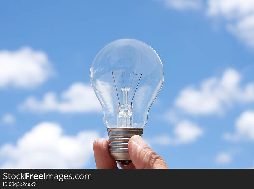 Hand holding light bulb in blue sky and cloud