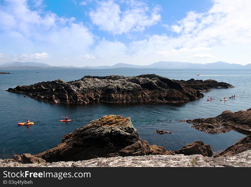 Kayaks in a scenic view in kerry ireland of rocks islands and sea with mountains against a beautiful blue cloudy sky. Kayaks in a scenic view in kerry ireland of rocks islands and sea with mountains against a beautiful blue cloudy sky