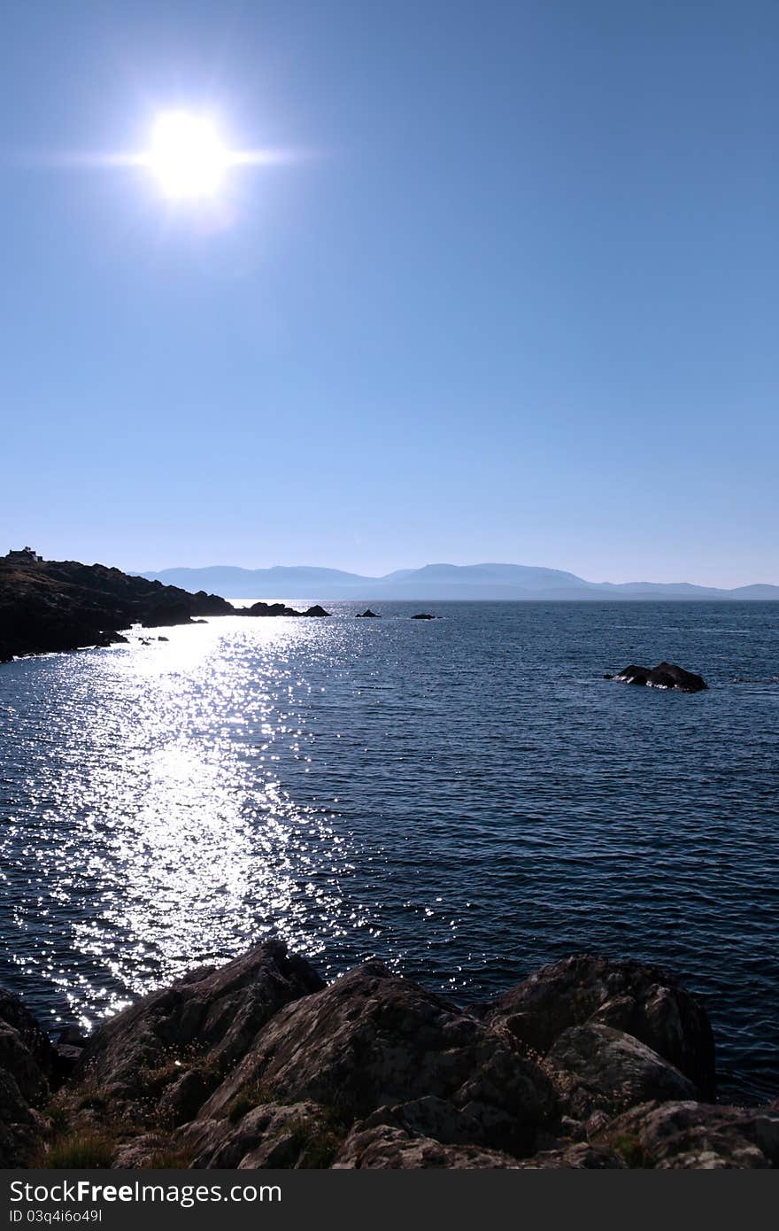 Scenic view in kerry ireland of rocks and sea with mountains against a beautiful bright sunny sky. Scenic view in kerry ireland of rocks and sea with mountains against a beautiful bright sunny sky