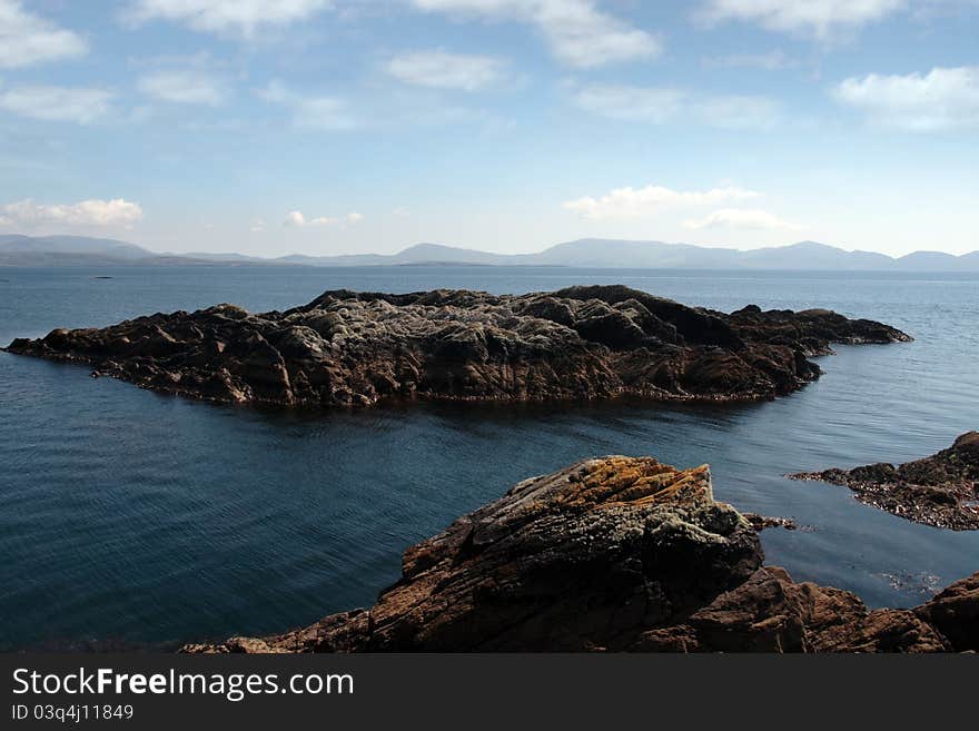 Scenic view in kerry ireland of rocks and sea with mountains against a beautiful blue cloudy sky. Scenic view in kerry ireland of rocks and sea with mountains against a beautiful blue cloudy sky