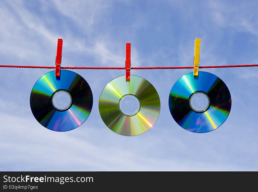 Three dvd and cd disks on clothes-line and sky. Three dvd and cd disks on clothes-line and sky