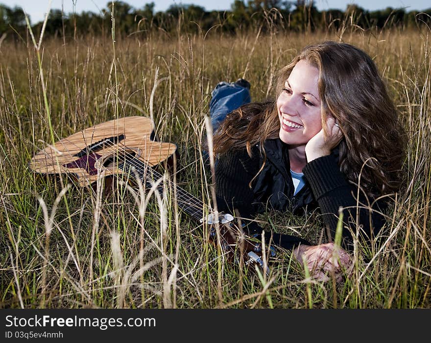 Young woman laying in field with her guitar. Young woman laying in field with her guitar