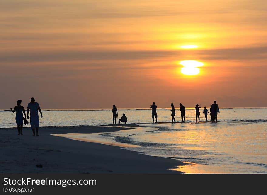 A view of a sunset in the Maldives with silouettes of people in the distance. A view of a sunset in the Maldives with silouettes of people in the distance.