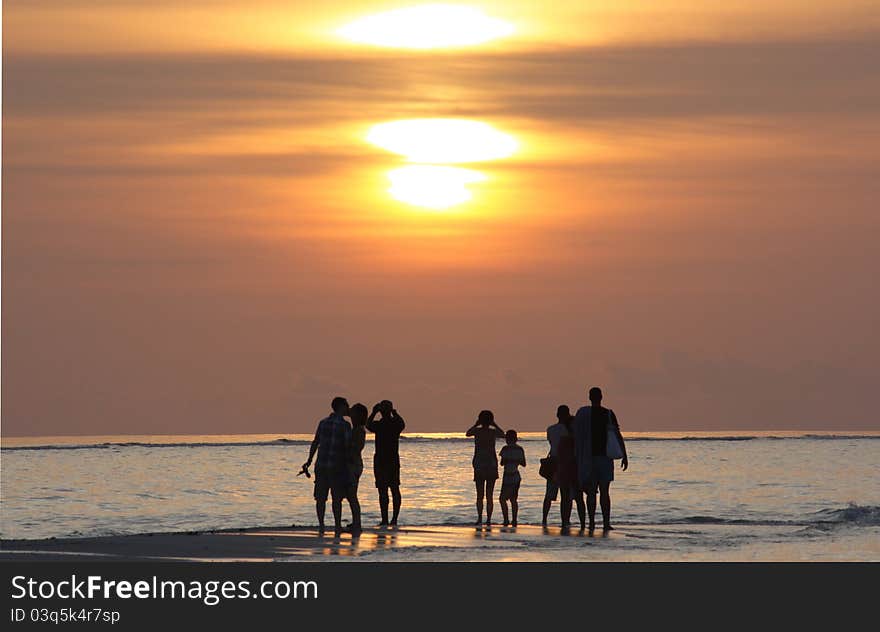 A view of a sunset in the Maldives with silhouettes of people in the distance. A view of a sunset in the Maldives with silhouettes of people in the distance.