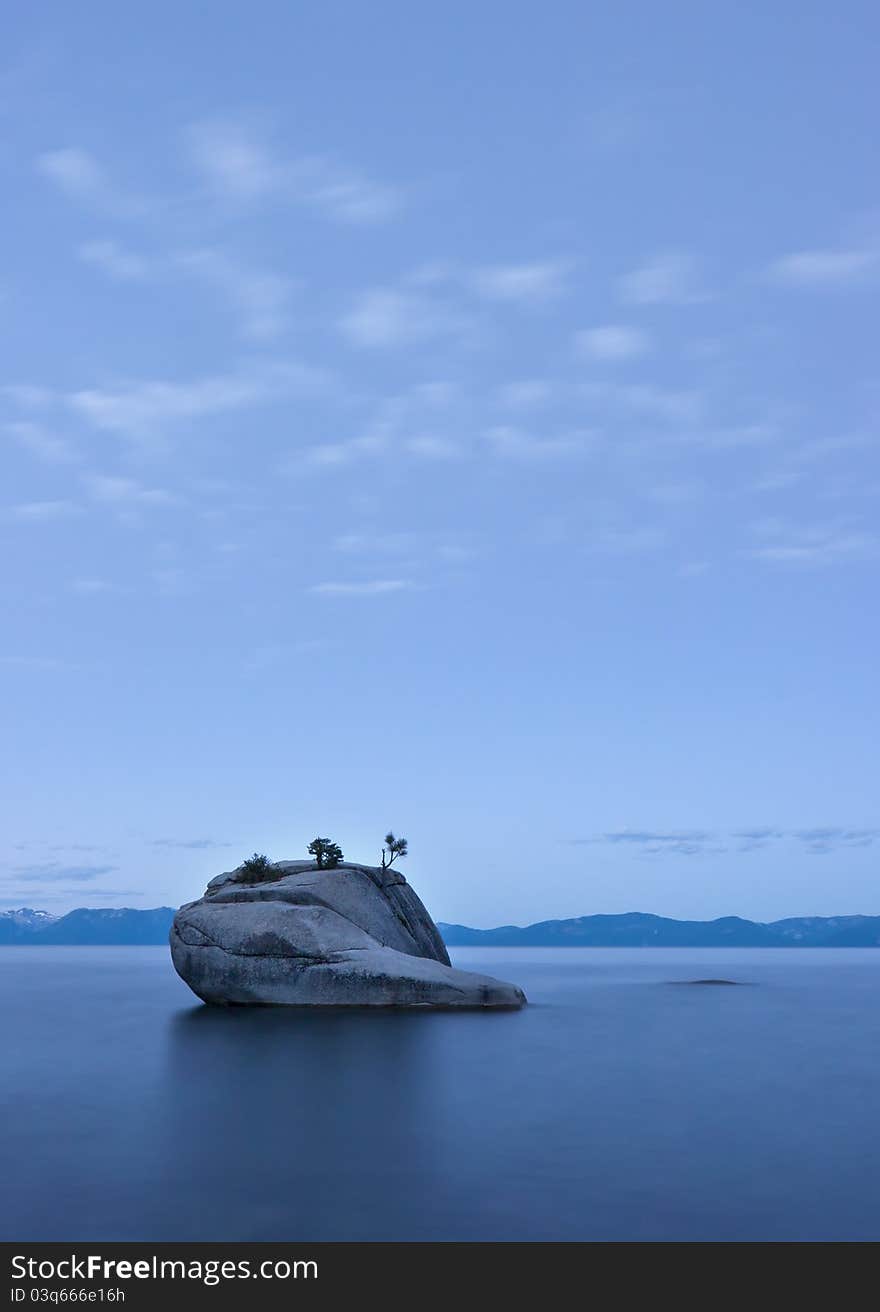 Single boulder with small trees growing out of it in Lake Tahoe, calm water blue sky and water. Single boulder with small trees growing out of it in Lake Tahoe, calm water blue sky and water