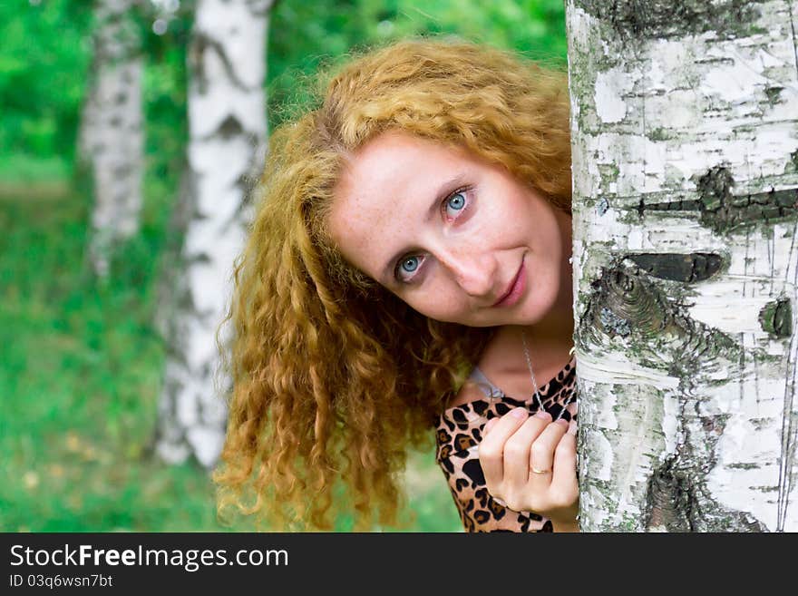 Beautiful girl looking out behind the tree outdoor