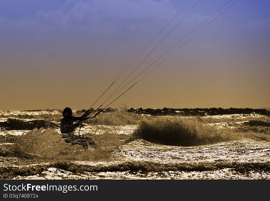 A Kite boarder in the sunset ride the surf on the wave in Capo Miseno, Italy. Backlight. A Kite boarder in the sunset ride the surf on the wave in Capo Miseno, Italy. Backlight.