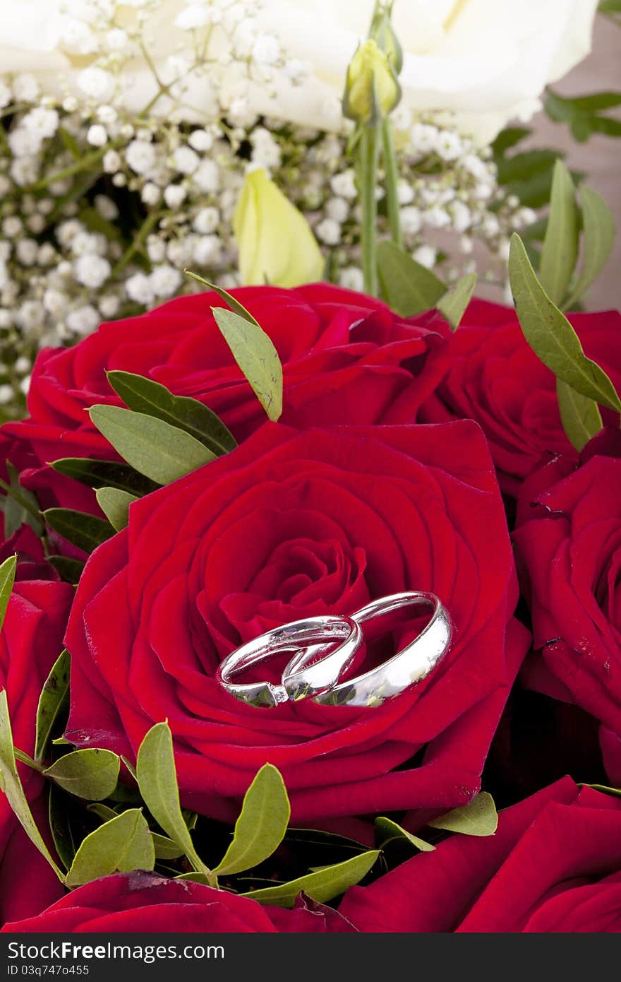 Studio-shot of white gold wedding rings on a bridal bouquet with red roses.