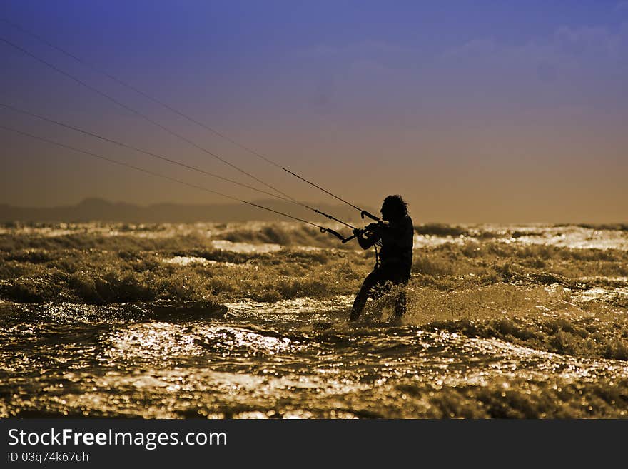 A Kite boarder in the sunset ride the surf on the wave in Capo Miseno, Italy. Backlight. A Kite boarder in the sunset ride the surf on the wave in Capo Miseno, Italy. Backlight.