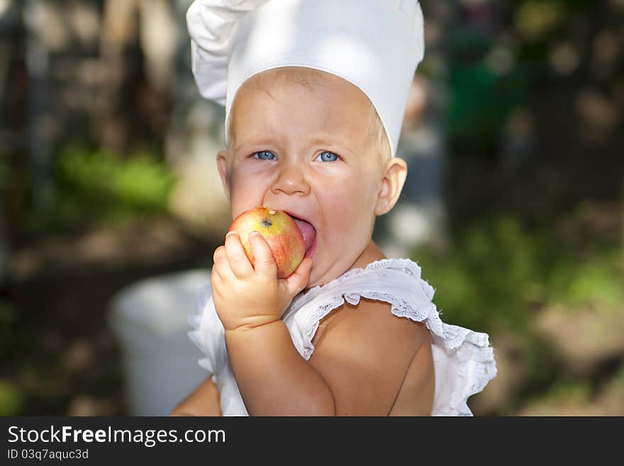 Little baby in the cook hat with an apple. Little baby in the cook hat with an apple.