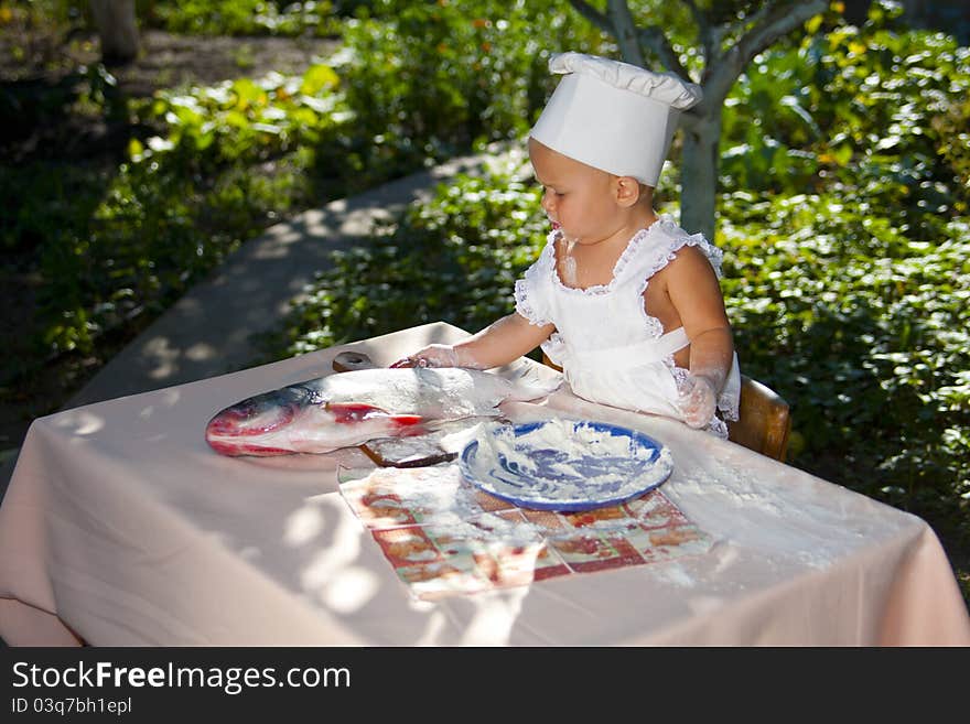 Cute little baby in cook-hat is preparing big fish in the garden. Cute little baby in cook-hat is preparing big fish in the garden.