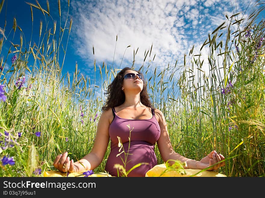 Pregnant woman on green grass field under blue sky in summer