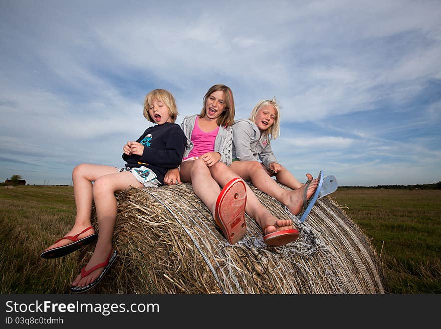 Three smilling children seated on bales of straw. Three smilling children seated on bales of straw