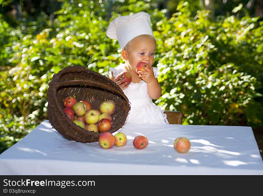 Cute small baby in cook hat and the big wicker basket of apples. Cute small baby in cook hat and the big wicker basket of apples.