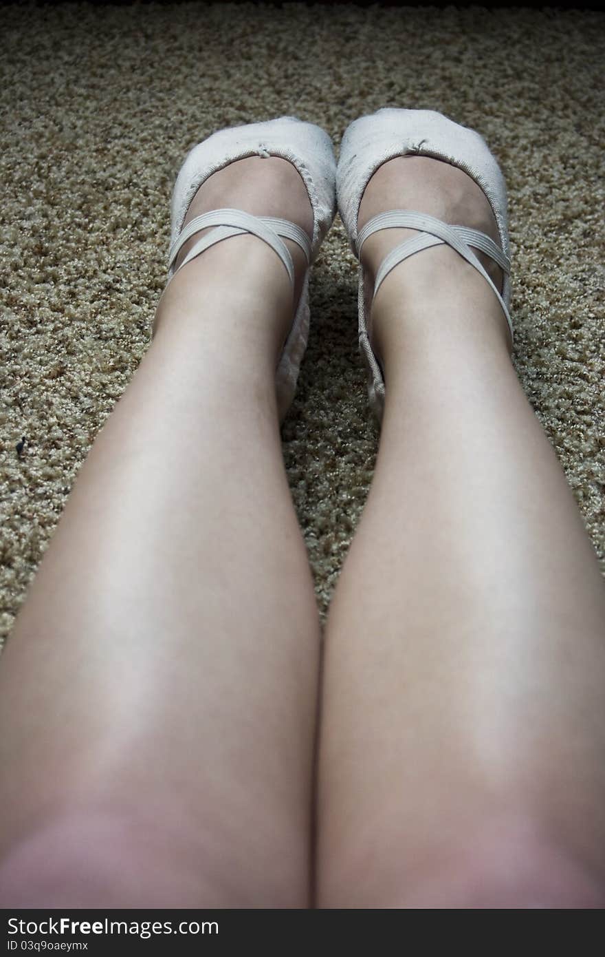 The bare outstretched legs of a ballet dancer wearing pink canvas ballet flats. The bare outstretched legs of a ballet dancer wearing pink canvas ballet flats.