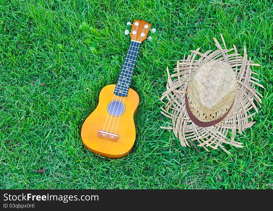 Hawaiian traditional instrument ukulele guitar with hat on green grass. Hawaiian traditional instrument ukulele guitar with hat on green grass