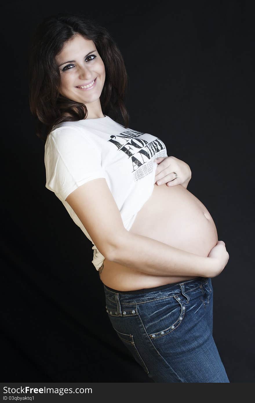 Pregnant woman with a jeans and white T-shirt standing on a black background. Pregnant woman with a jeans and white T-shirt standing on a black background