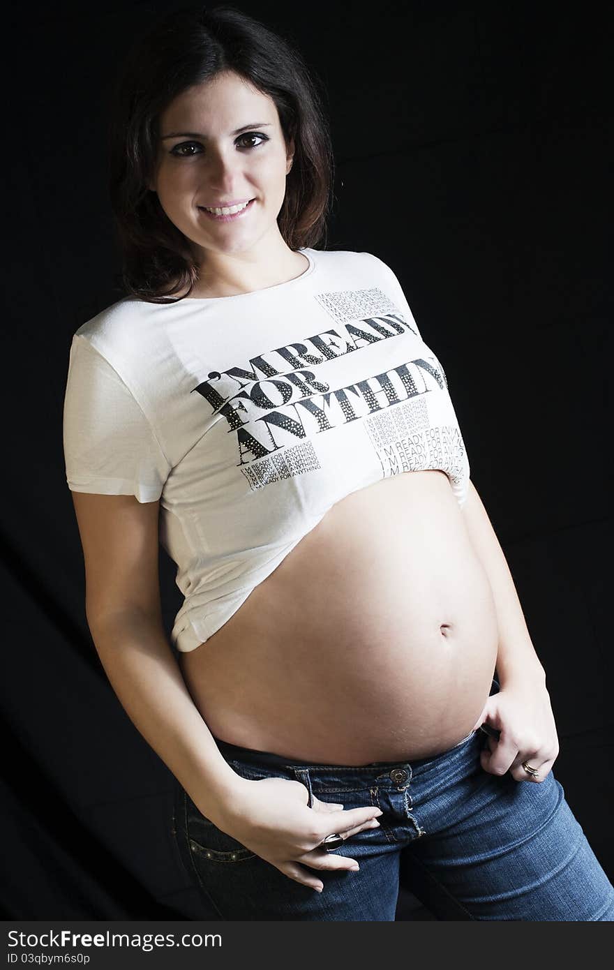 Pregnant woman with a jeans and white T-shirt standing on a black background. Pregnant woman with a jeans and white T-shirt standing on a black background