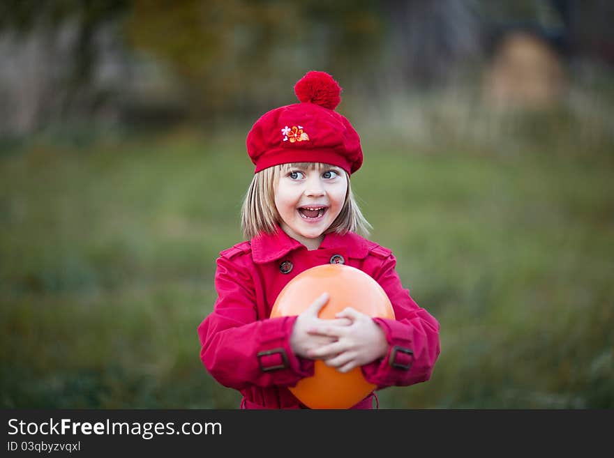 Girl with surprised face, smilling, wears in a red cap and red coat, holding orange balloon. Girl with surprised face, smilling, wears in a red cap and red coat, holding orange balloon