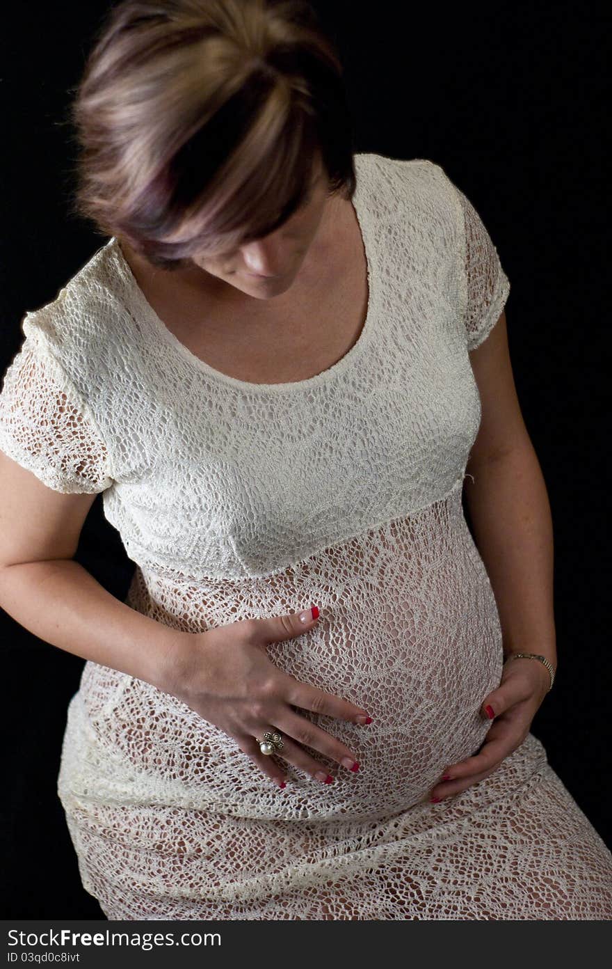 Young pregnant woman wearing lace dress looking down at her belly and isolated on black background