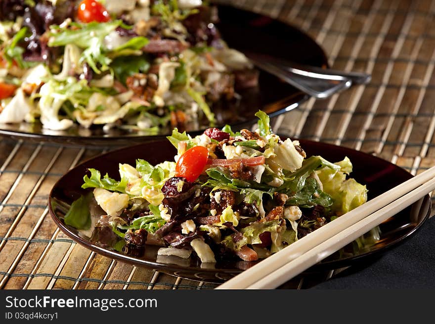 Fresh chopped salad on a black plate with chop sticks in the foreground. Salad serving dish in the background.