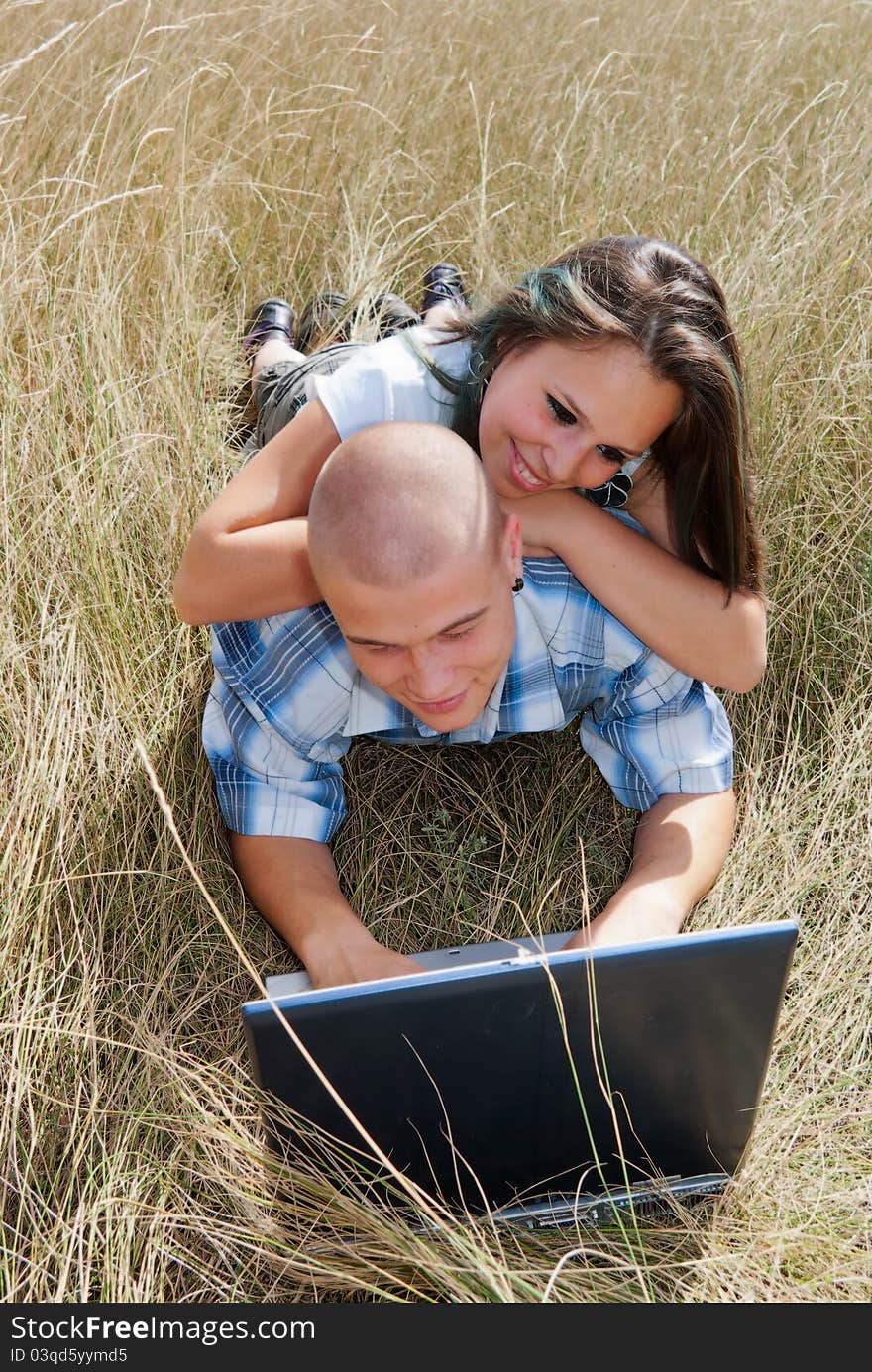 Happy boy and girl sitting on the grass and use a netbook on the Internet. Happy boy and girl sitting on the grass and use a netbook on the Internet