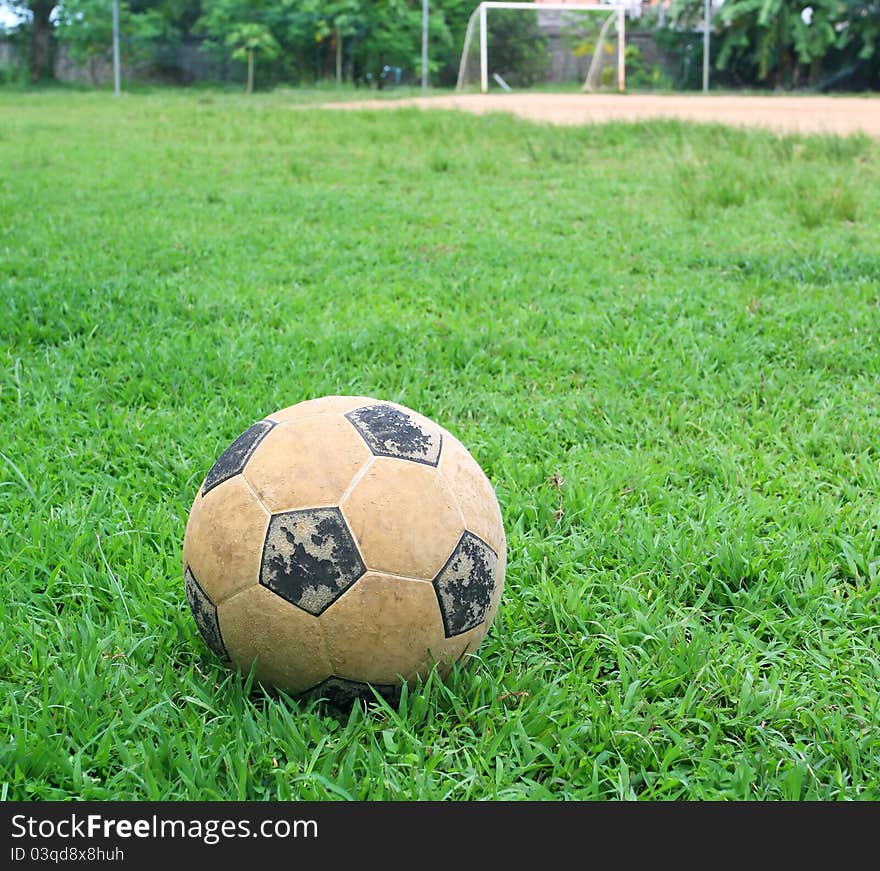 An old soccer ball on ground, goal is the background. An old soccer ball on ground, goal is the background