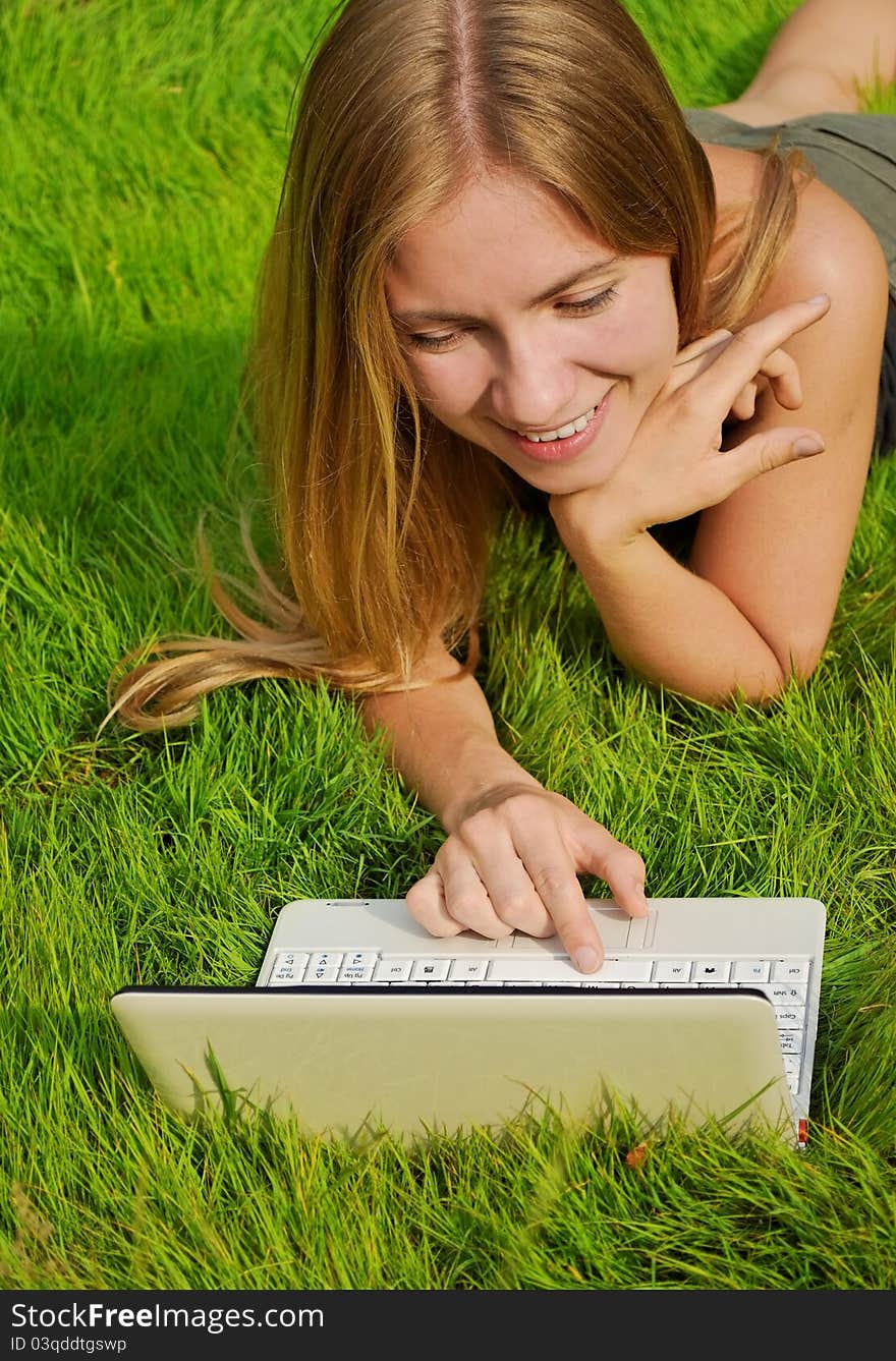 Smiling girl on lawn working on laptop