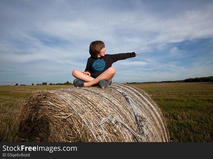 Boy sitting on hay bales, pointing on something. Boy sitting on hay bales, pointing on something