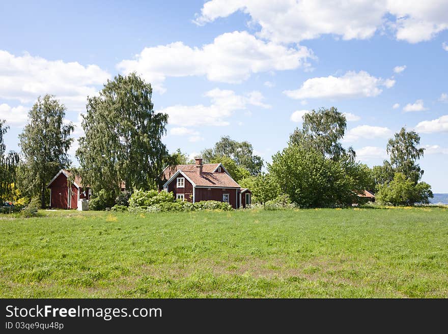 Small red house in a green field. House is surrounded by beautiful trees. Small red house in a green field. House is surrounded by beautiful trees.