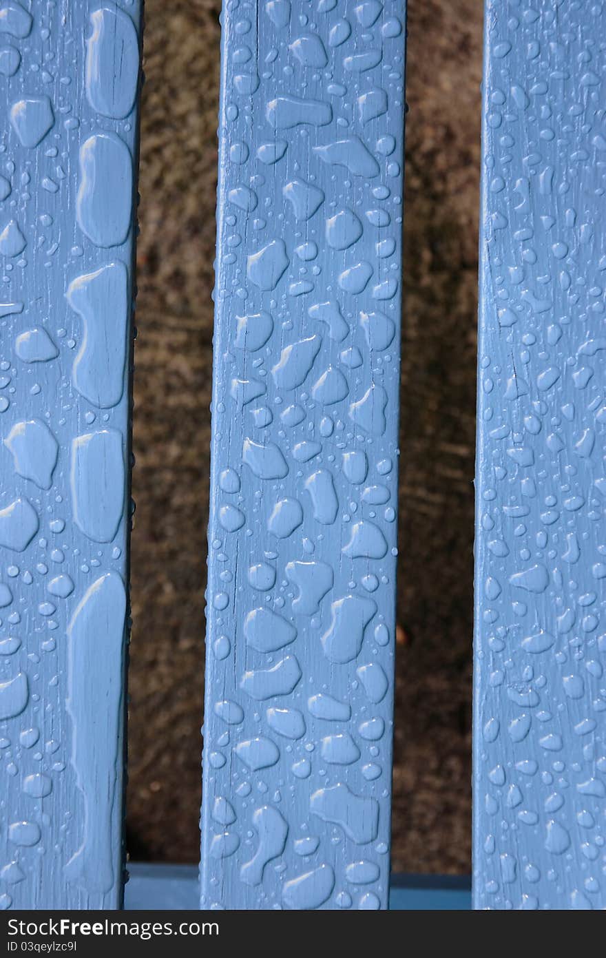 A wooden garden chair with rain drops on the surface. A wooden garden chair with rain drops on the surface