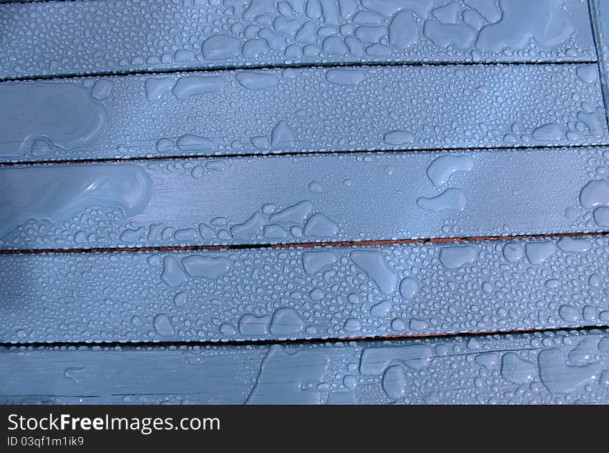 A wooden garden chair with rain drops on the surface. A wooden garden chair with rain drops on the surface