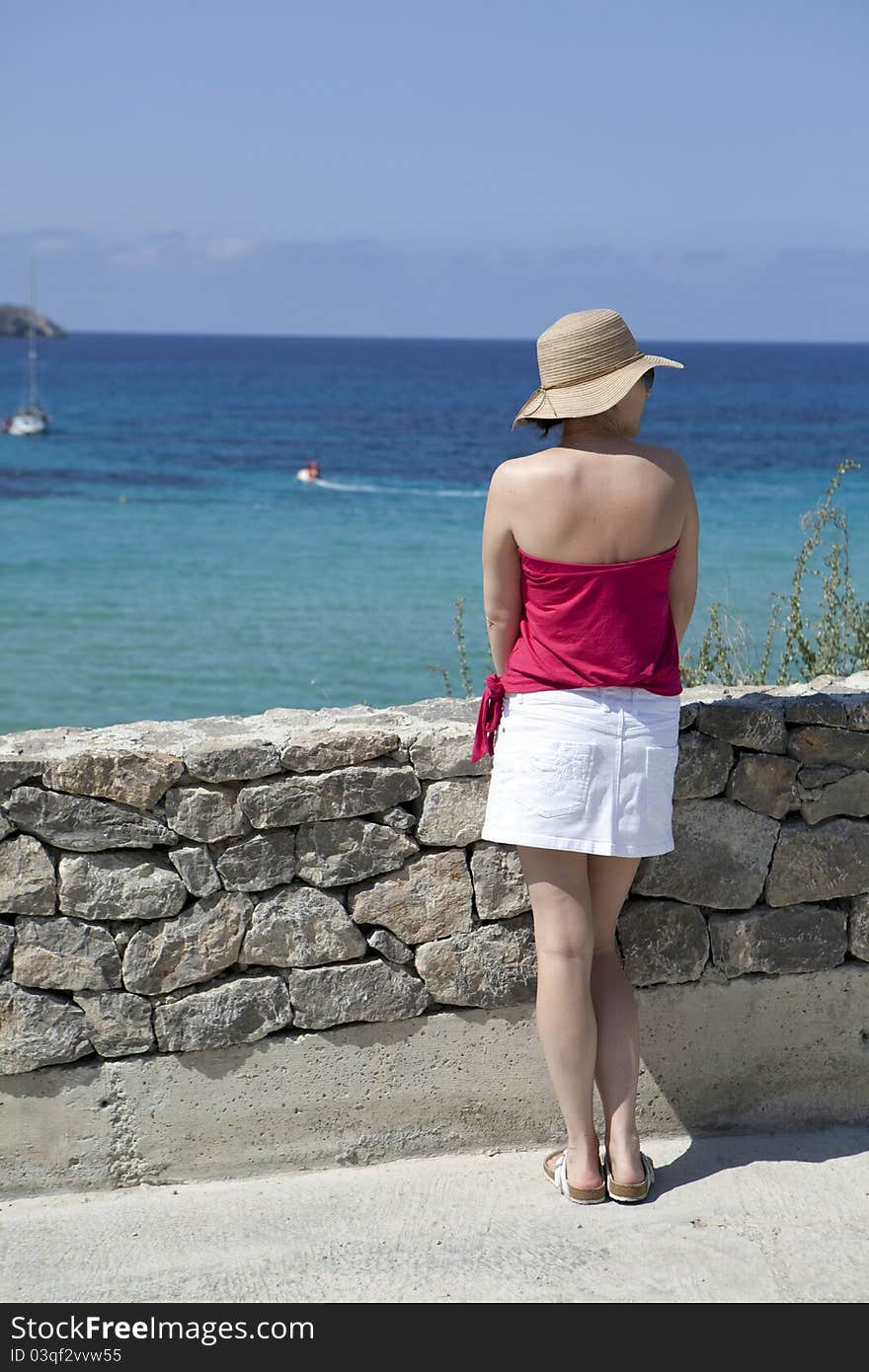 A woman in a straw hat looking out to sea.