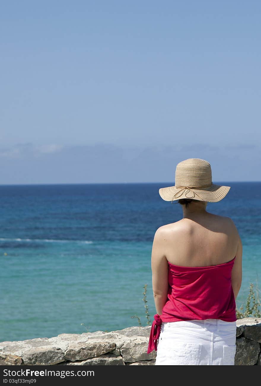 A woman in a straw hat looking out to sea.