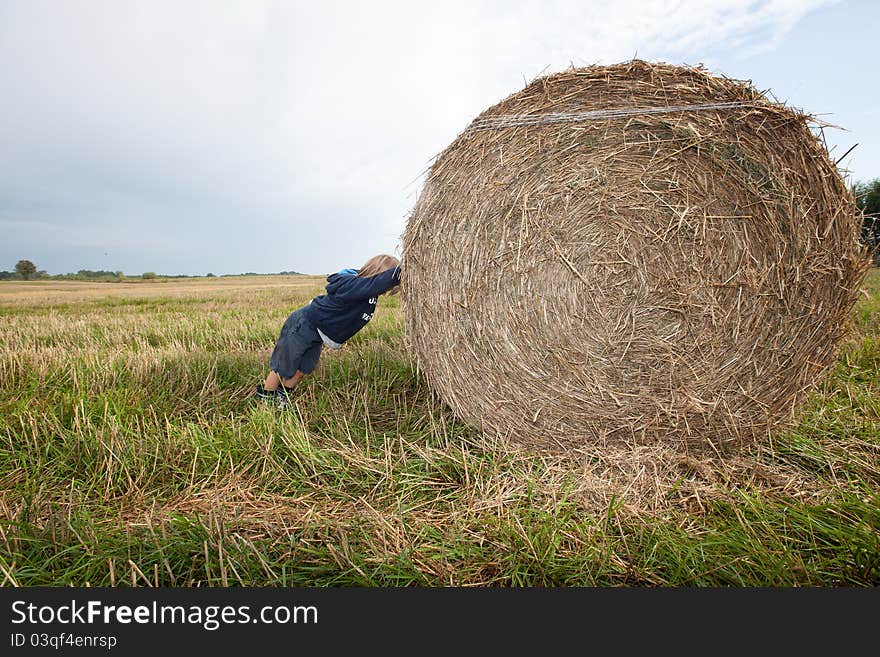 A small boy pushing huge bales of hay. A small boy pushing huge bales of hay