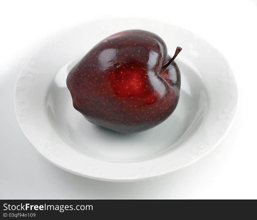 Dark red apple over white plate on white background. Dark red apple over white plate on white background