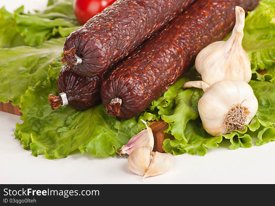 Salami with lettuce, garlic and tomatoes on white background. Salami with lettuce, garlic and tomatoes on white background