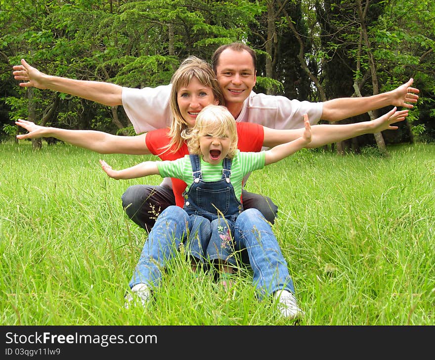 Happy family with little girl sits on meadow and lauthing