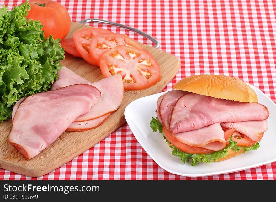 Ham sandwich with lettuce and tomato on a plate with ham, lettuce and tomato on a cutting board. Ham sandwich with lettuce and tomato on a plate with ham, lettuce and tomato on a cutting board