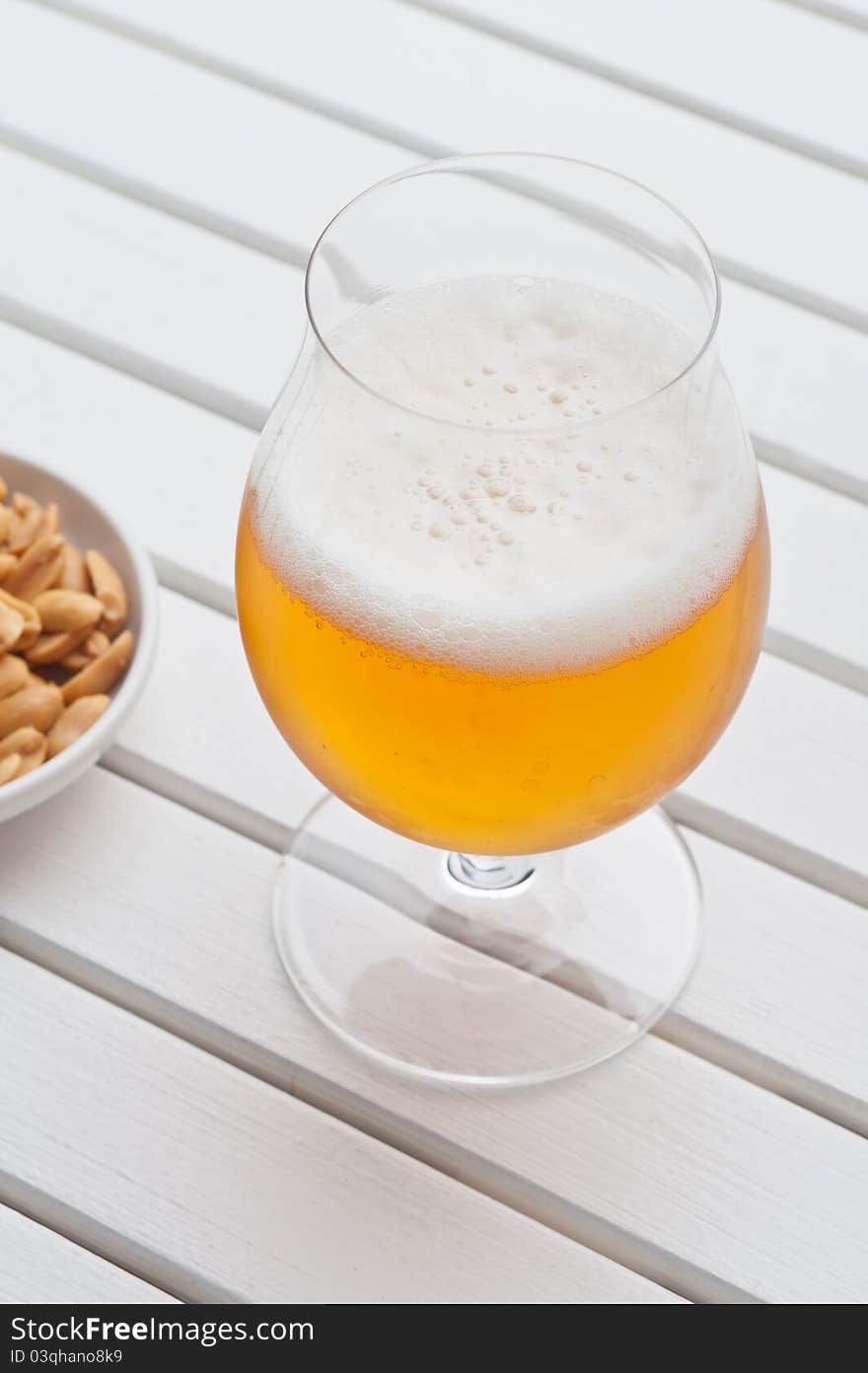 Beer with peanuts on a white table