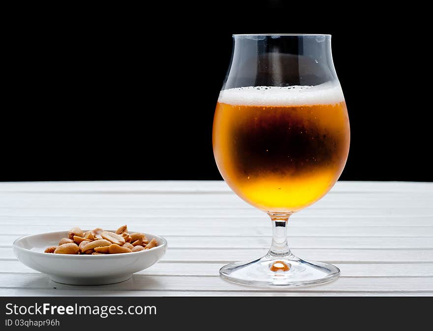 Beer with peanuts on white table