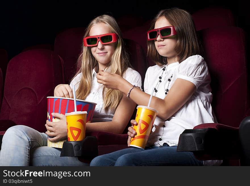 Two girls look three-dimensional cinema, sitting in the glasses, eat popcorn, drink drink. Two girls look three-dimensional cinema, sitting in the glasses, eat popcorn, drink drink