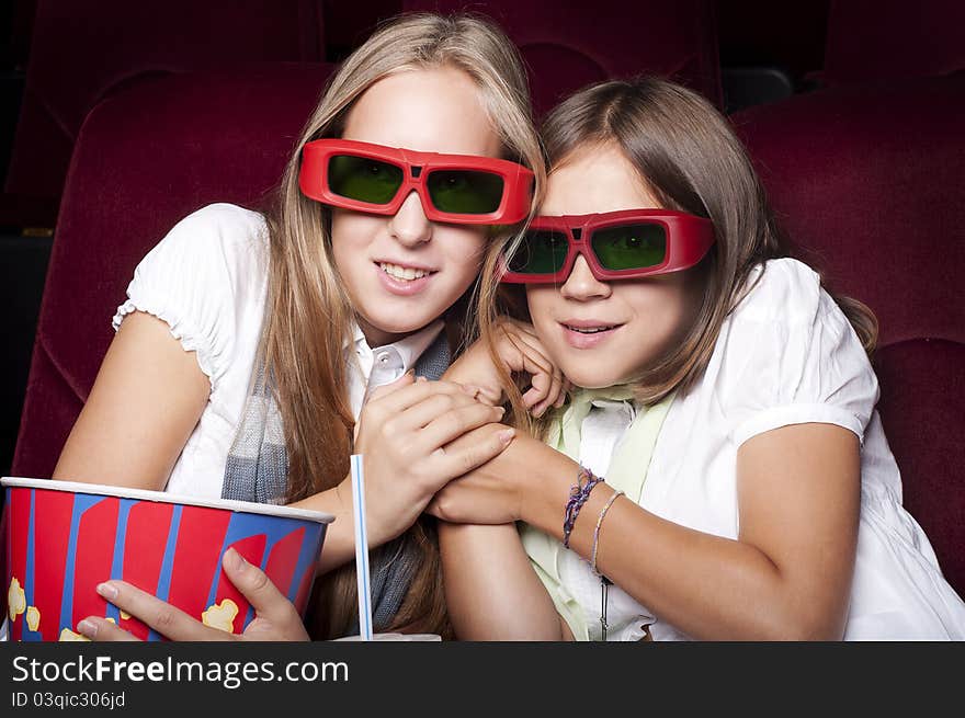 Two girls look three-dimensional cinema, sitting in the glasses, eat popcorn, drink drink. Two girls look three-dimensional cinema, sitting in the glasses, eat popcorn, drink drink