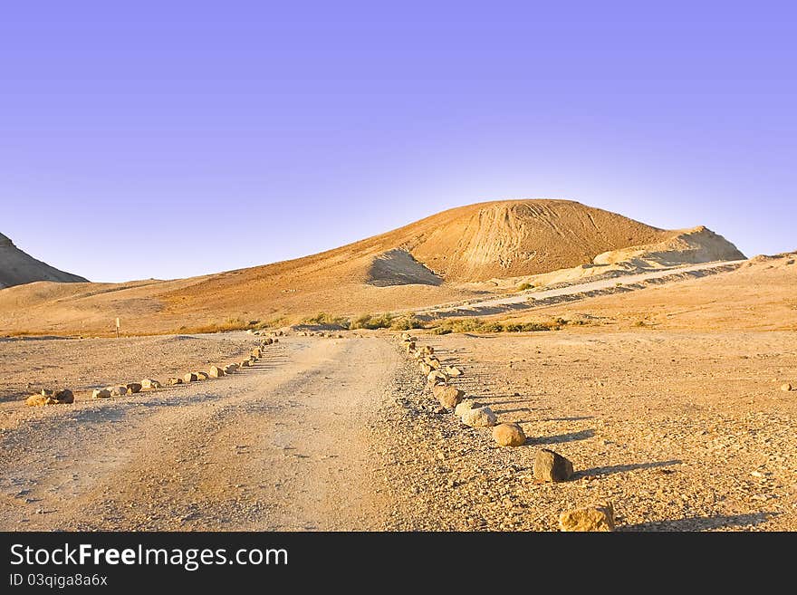 A stone-boarded track leading to a sight point in desert faces a golden hill and blue skies. A stone-boarded track leading to a sight point in desert faces a golden hill and blue skies.